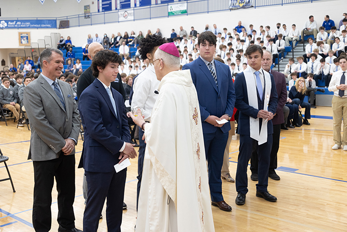 Auxiliary Bishop Donald F. Hanchon welcomes four students into the Church at Catholic Central all-school Mass